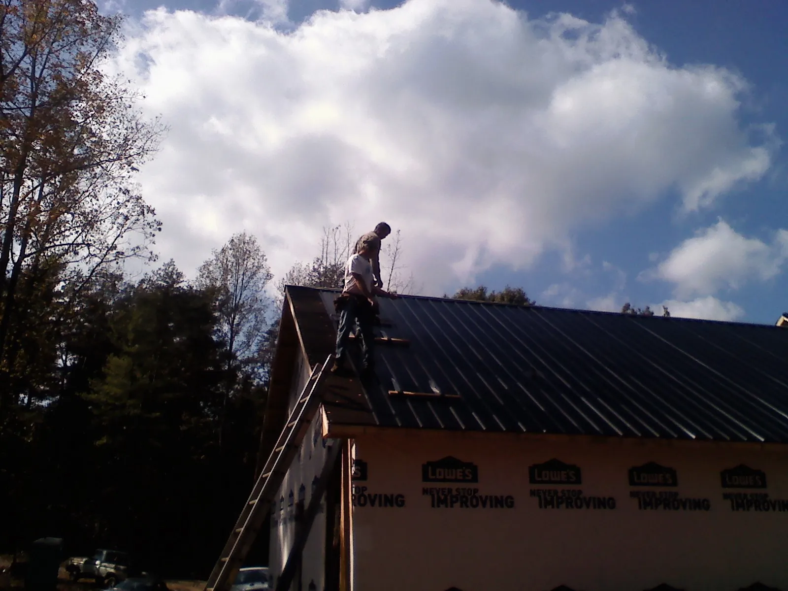 Roofer fastening dark metal panels high against a cloudy sky, from a Roof Inspection job in Edwards